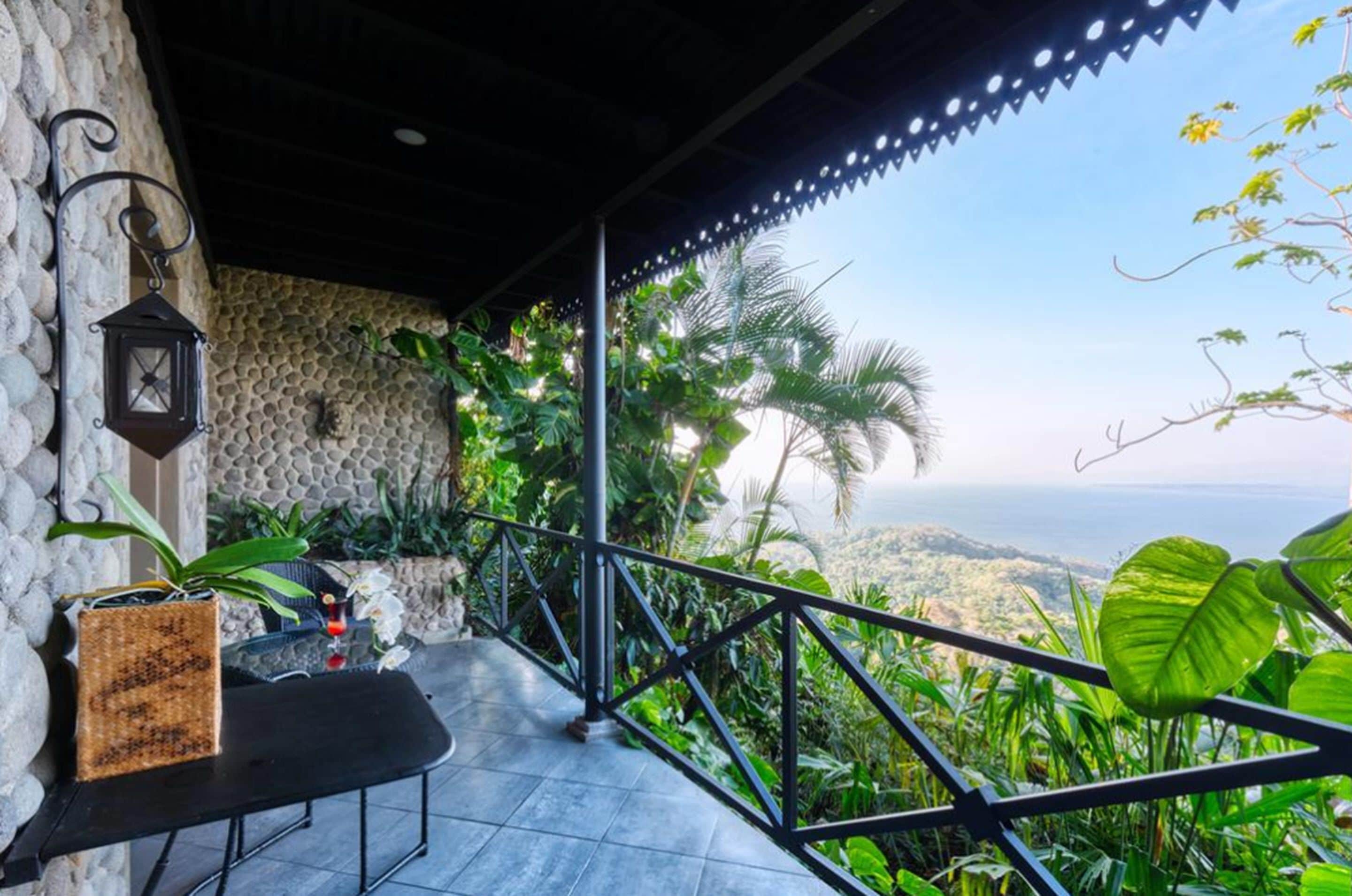 A balcony with a stone wall, a hanging lantern, and lush greenery.