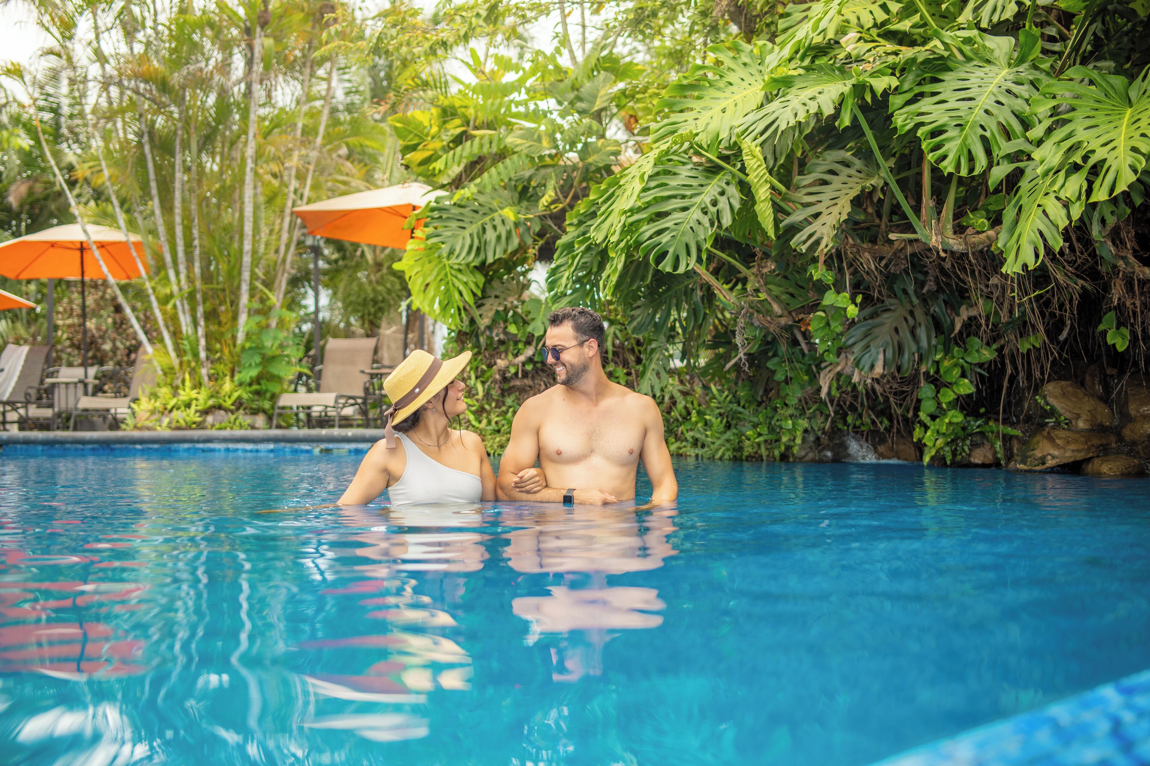 A swimming pool with lounge chairs and umbrellas, surrounded by lush greenery.