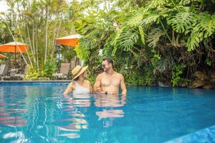 A swimming pool with lounge chairs and umbrellas, surrounded by lush greenery.