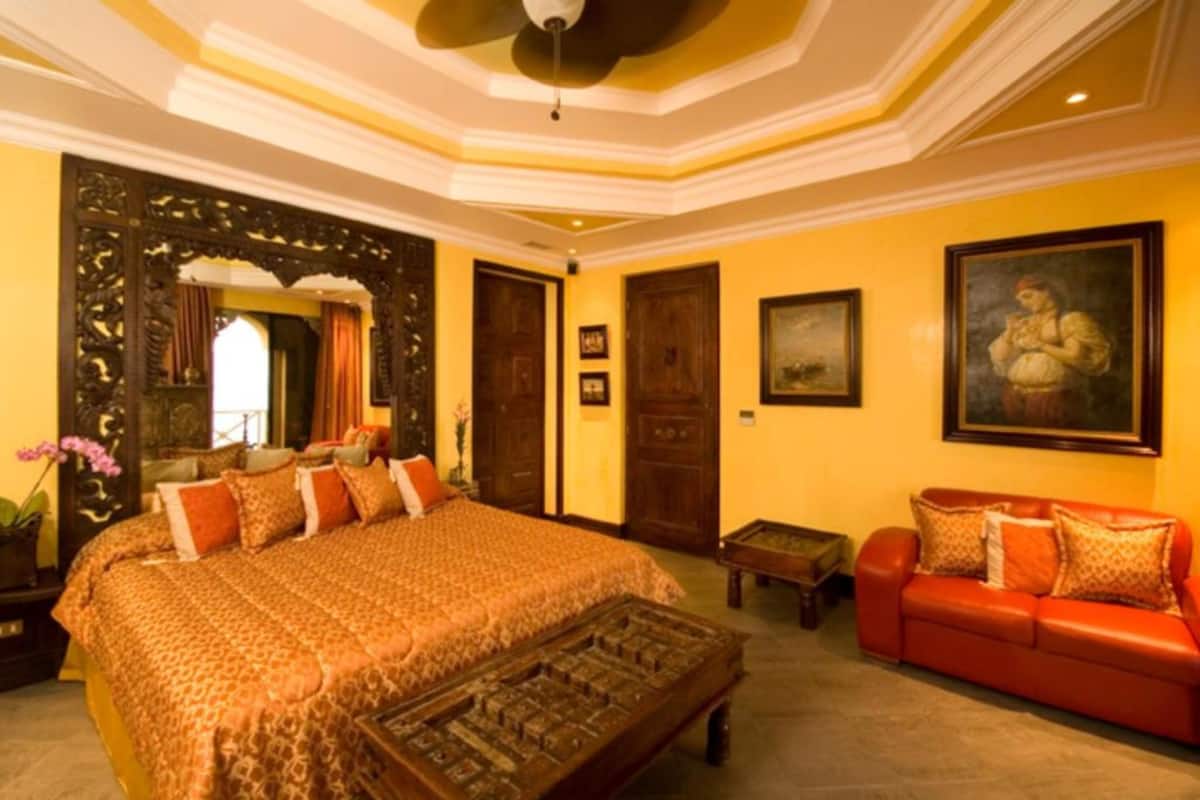 A hotel room with a large bed, a red sofa, a wooden coffee table, and a ceiling fan.