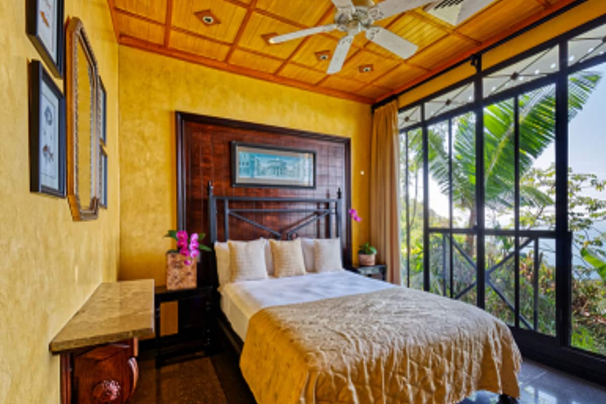 A bedroom with a large bed, wooden ceiling, and a view of greenery outside.