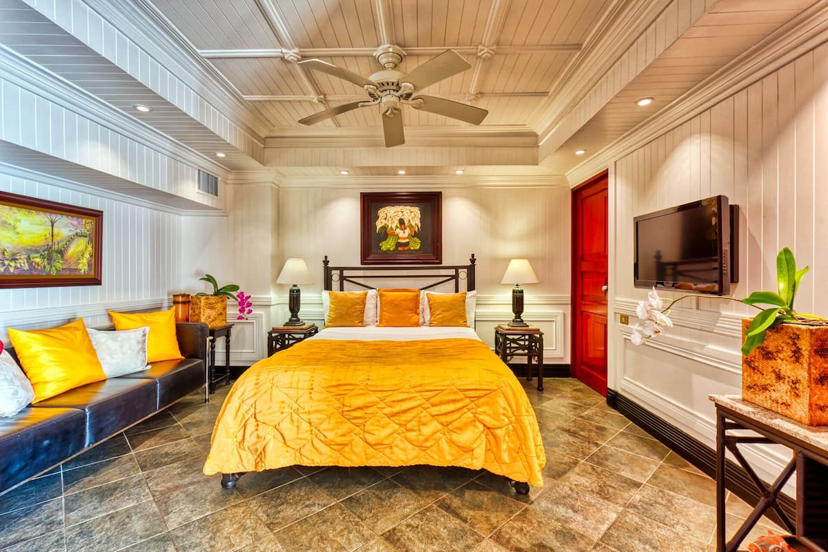 A hotel room with a large bed, two bedside tables, a ceiling fan, a TV, and a red door.