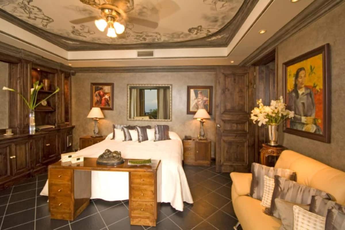 A spacious bedroom with a large bed, a wooden desk, a sofa, and a ceiling fan.