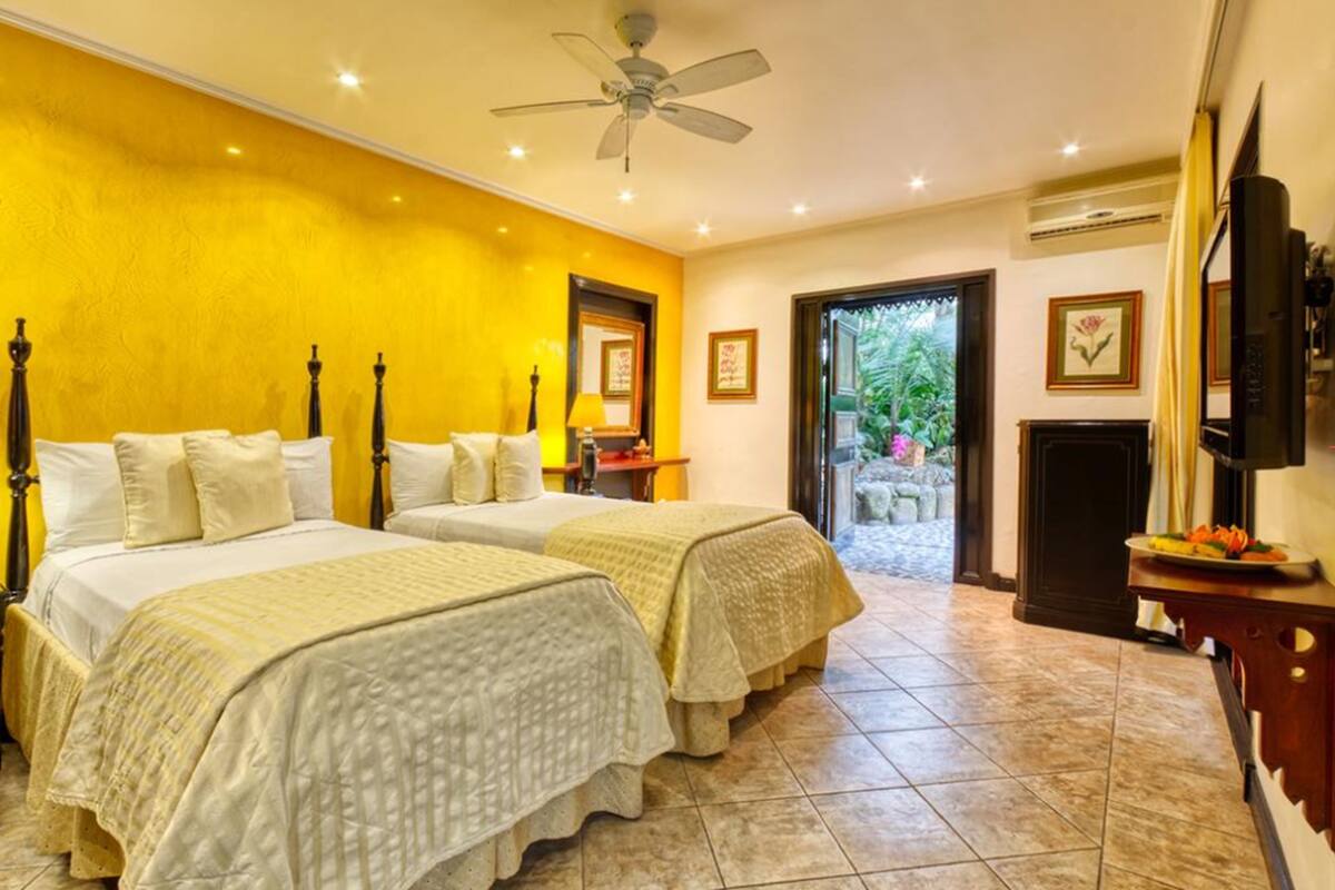 A hotel room with two beds, a ceiling fan, a TV, and a view of the outdoors.