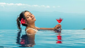 A person in a clear blue pool holding a red drink. - Hotel Villa Caletas (Tárcoles)