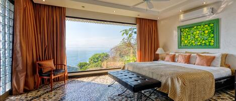 A spacious bedroom with a large bed, a bench, and a view of the ocean.