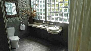 A bathroom with a stone wall, a toilet, a sink, and a window with a view of greenery.