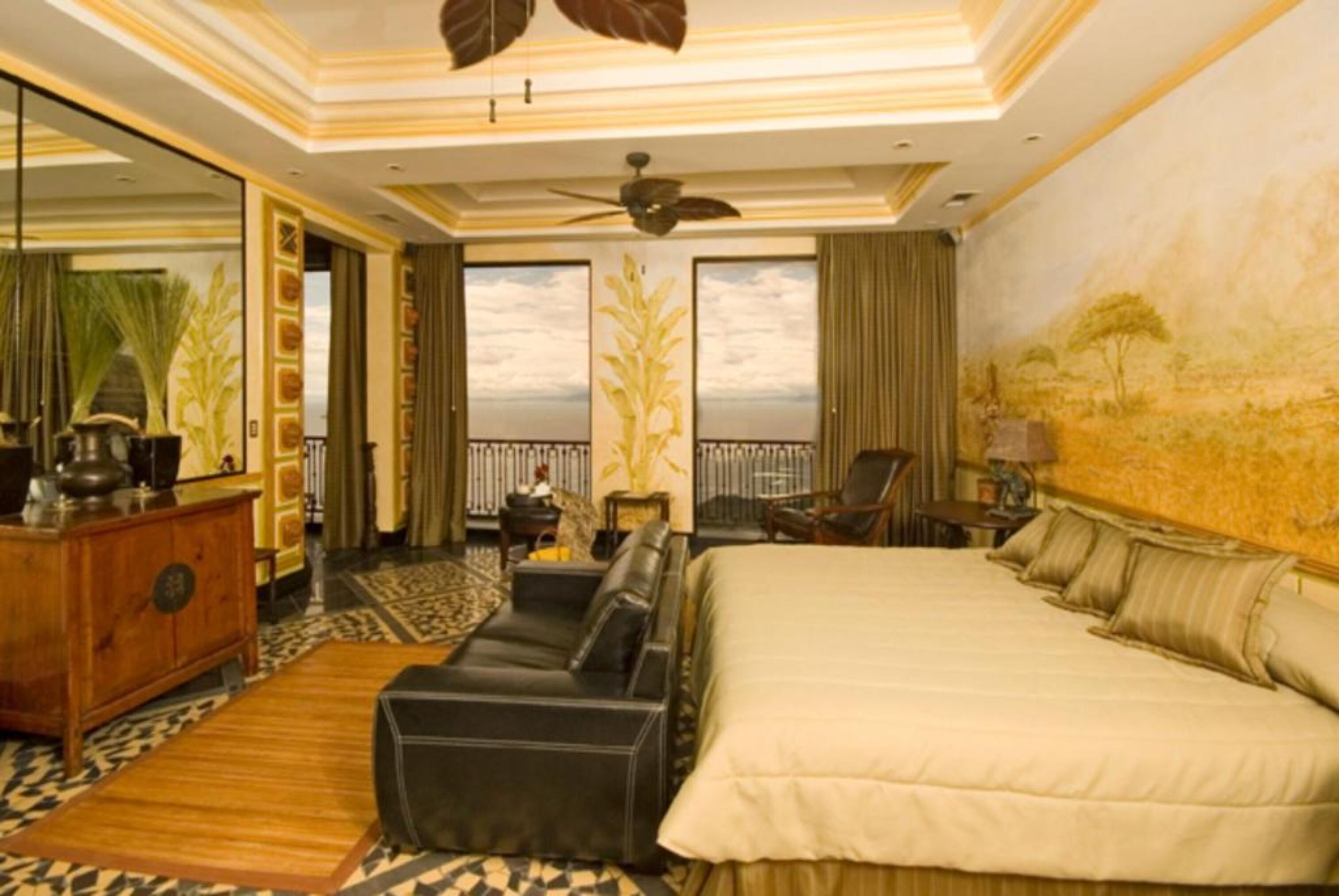 A spacious hotel room with a large bed, a sofa, a desk, and a balcony with a view.