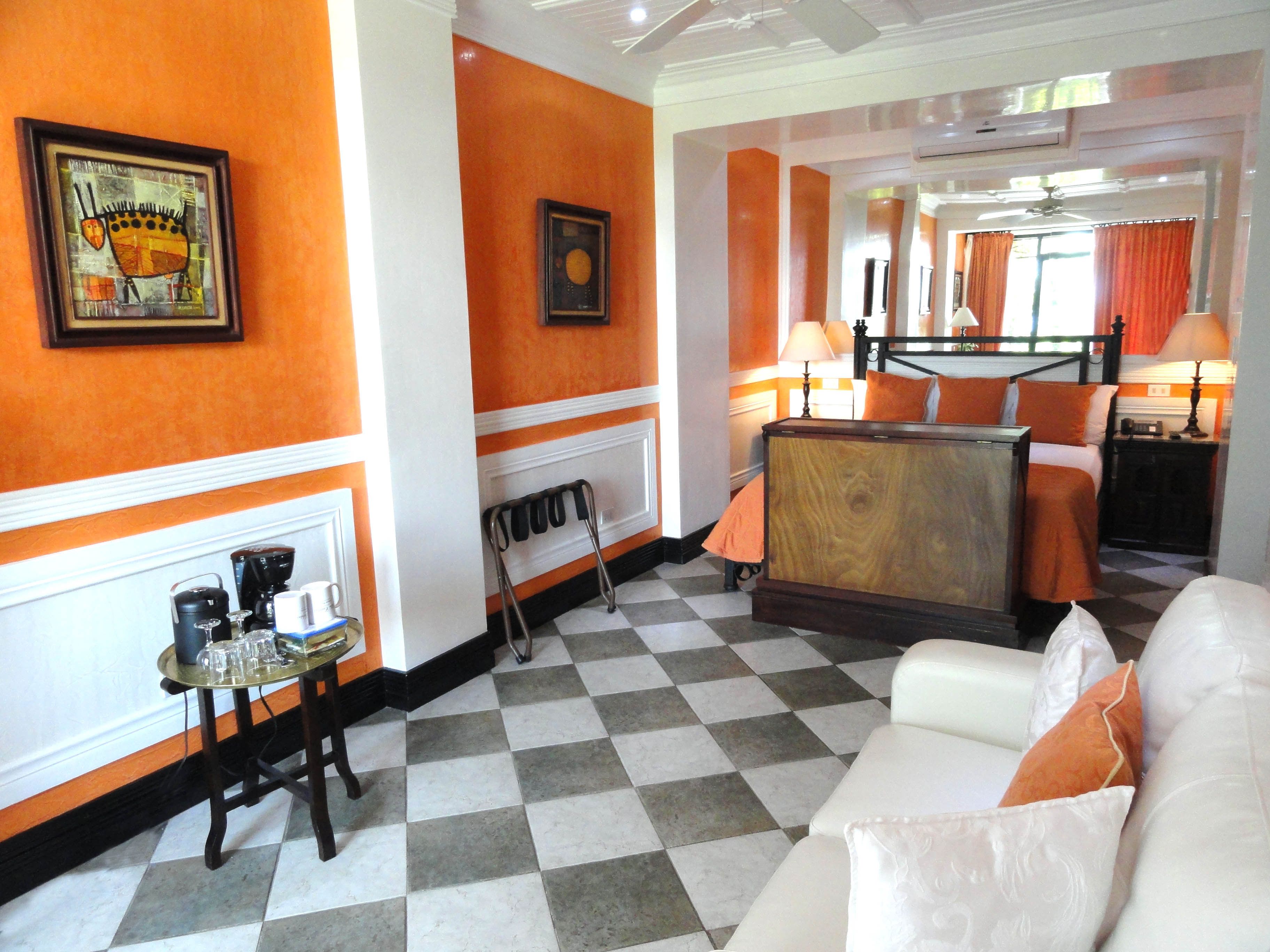 Un hall d’hôtel avec un sol à carreaux, des murs orange, un canapé, une table basse et un lit avec une literie orange.
