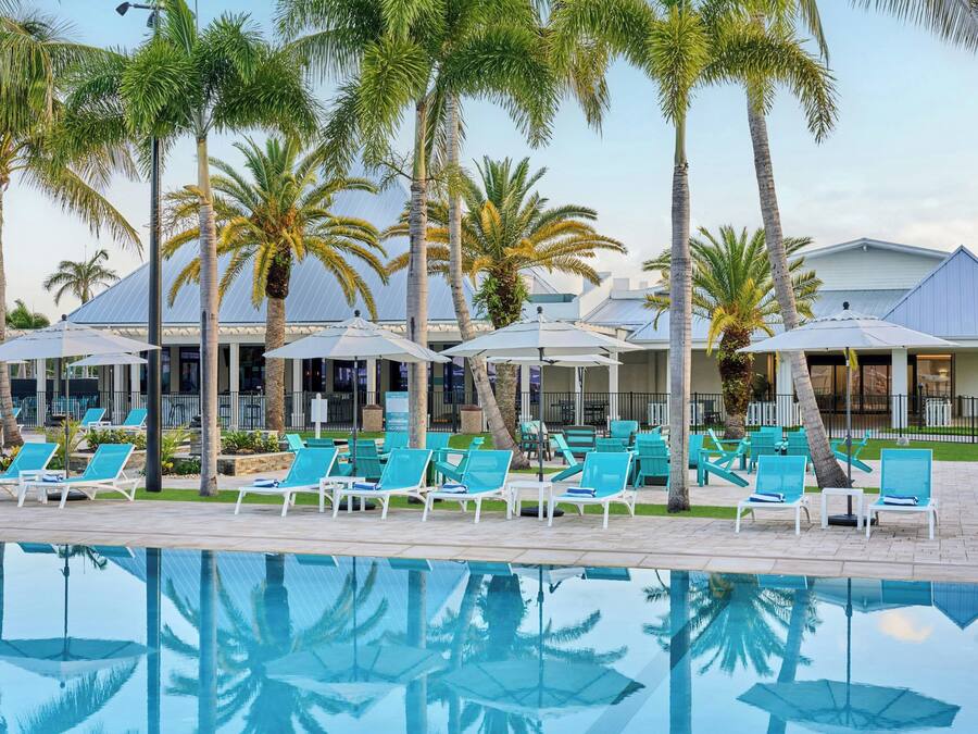 A poolside area with lounge chairs and umbrellas, surrounded by palm trees.