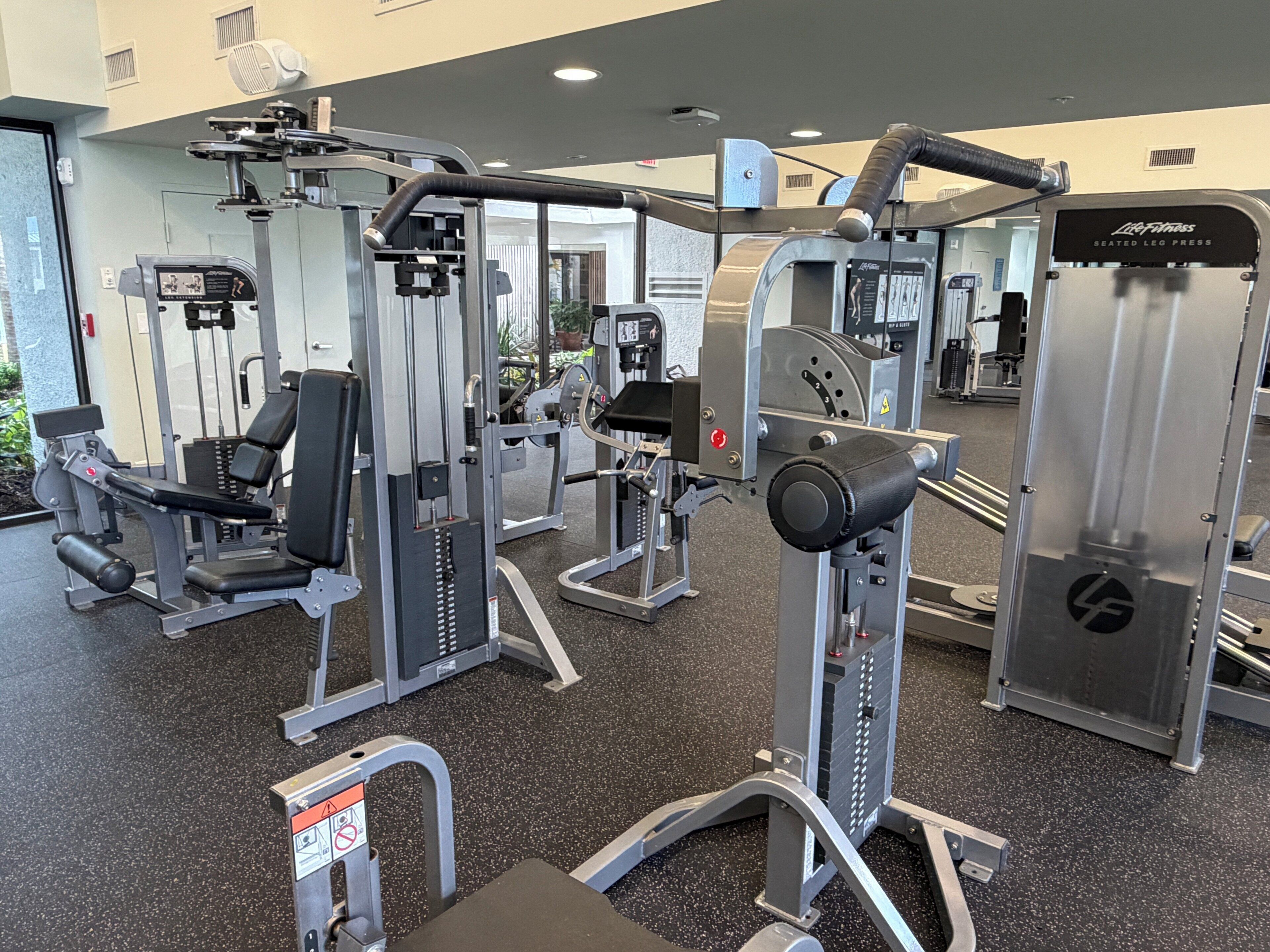 Un gimnasio con diversas máquinas de ejercicio, una prensa de piernas y un espejo grande.