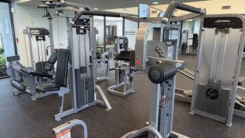 A gym with various exercise machines, a seated leg press, and a mirrored wall.