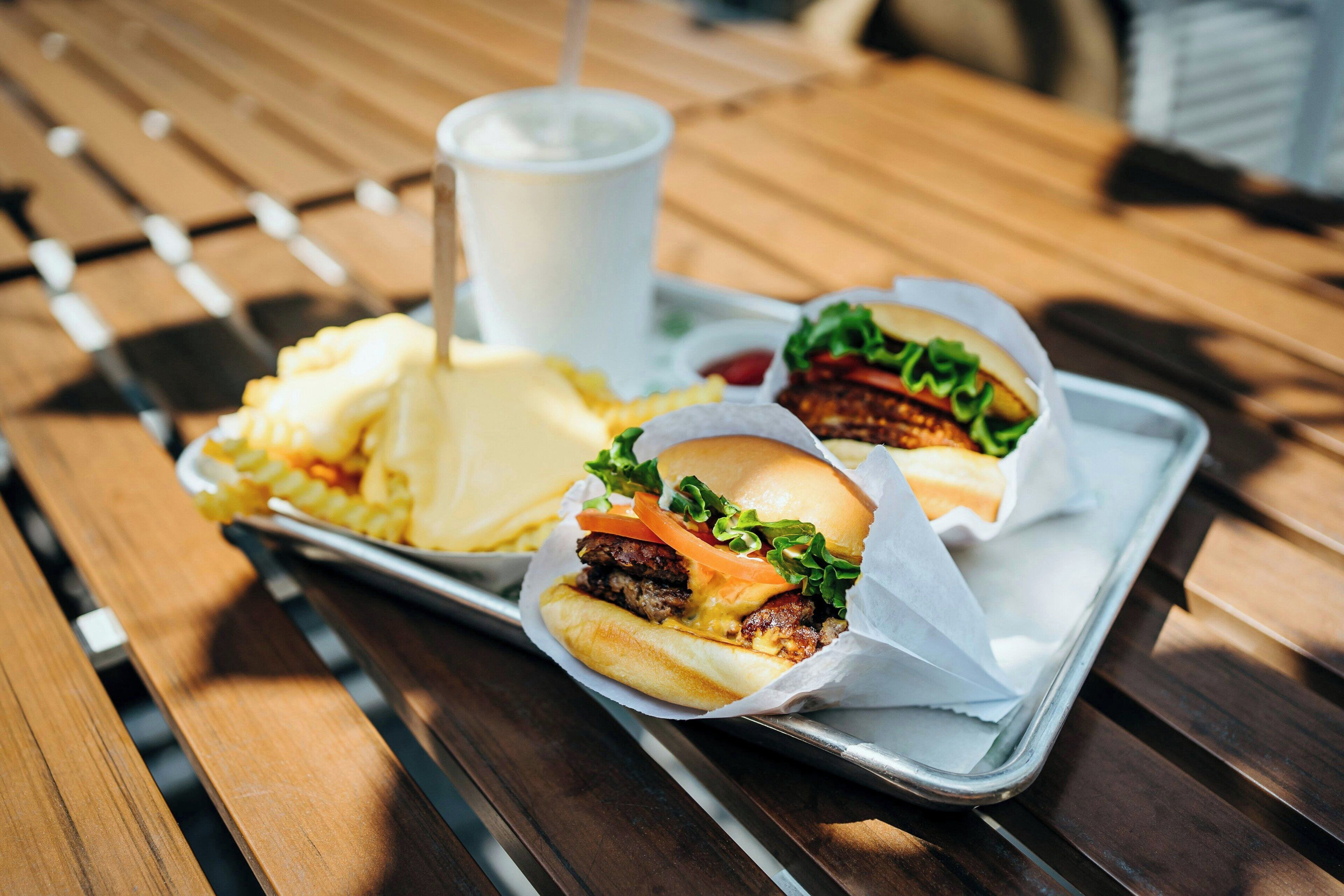 Een dienblad met twee burgers, friet en een drankje op een houten tafel.