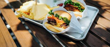 Een dienblad met twee burgers, friet en een drankje op een houten tafel.