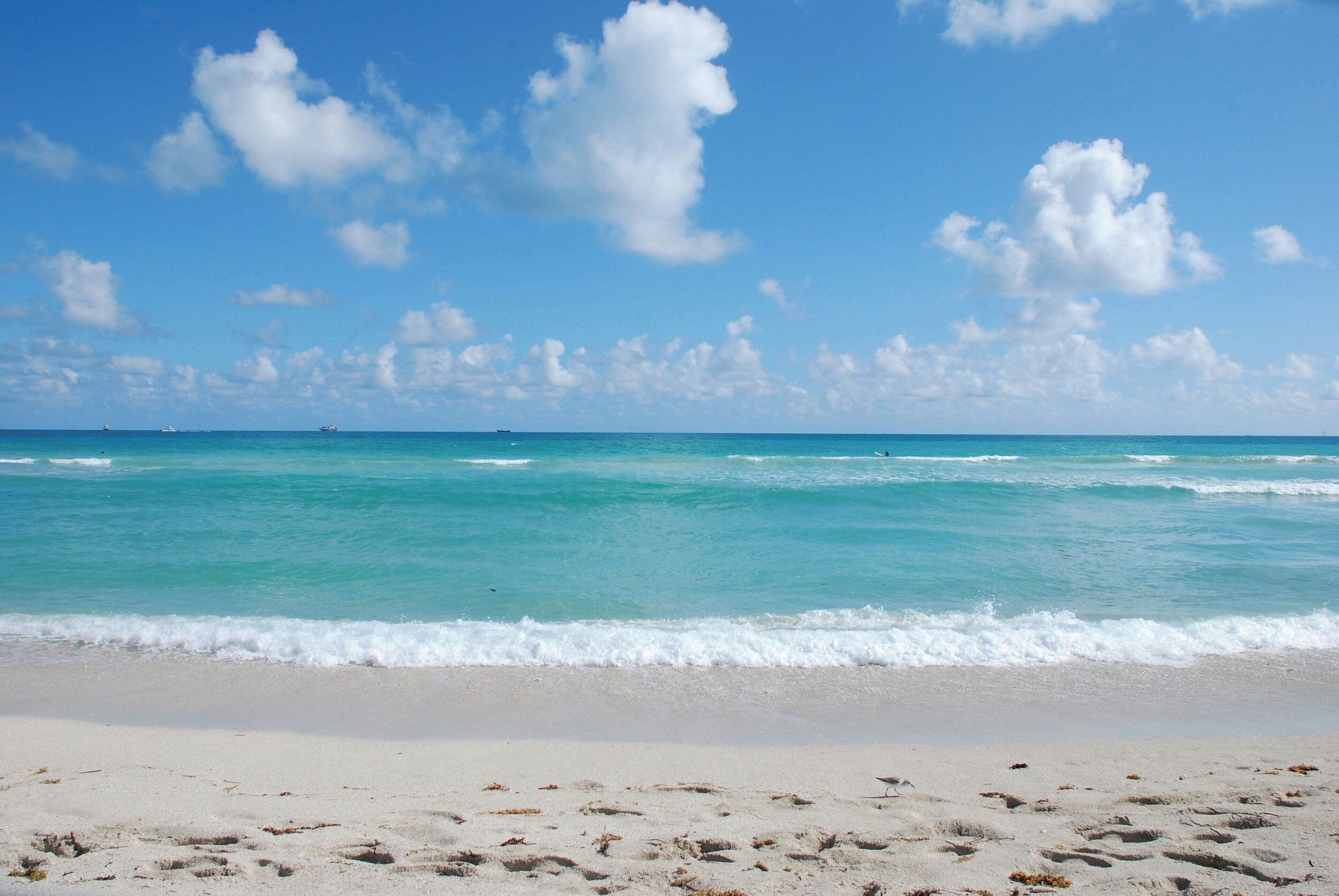 Une plage à l’eau turquoise et limpide, au sable blanc, parsemée de quelques empreintes de pas.