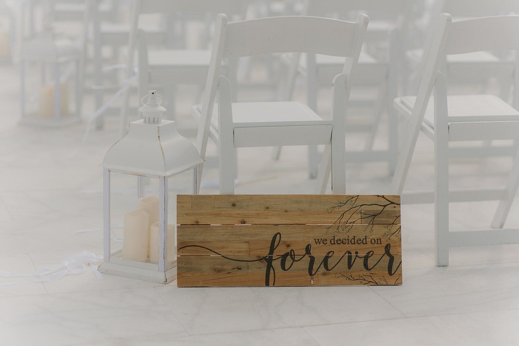 Une rangée de chaises blanches et un panneau en bois portant l’inscription « nous avons décidé de nous aimer pour toujours », le tout dans un décor rustique.