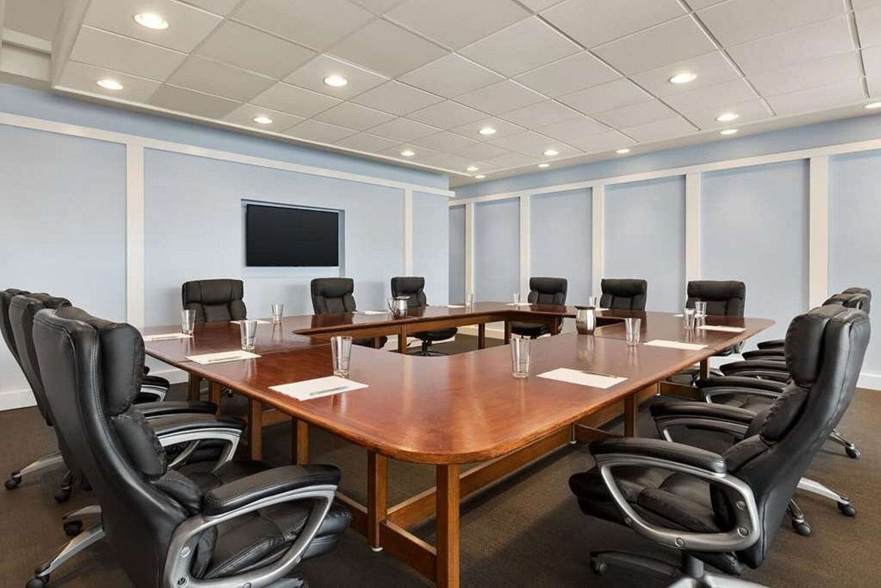 Une salle de conférence avec une longue table en bois, des fauteuils en cuir noir et un grand écran mural.