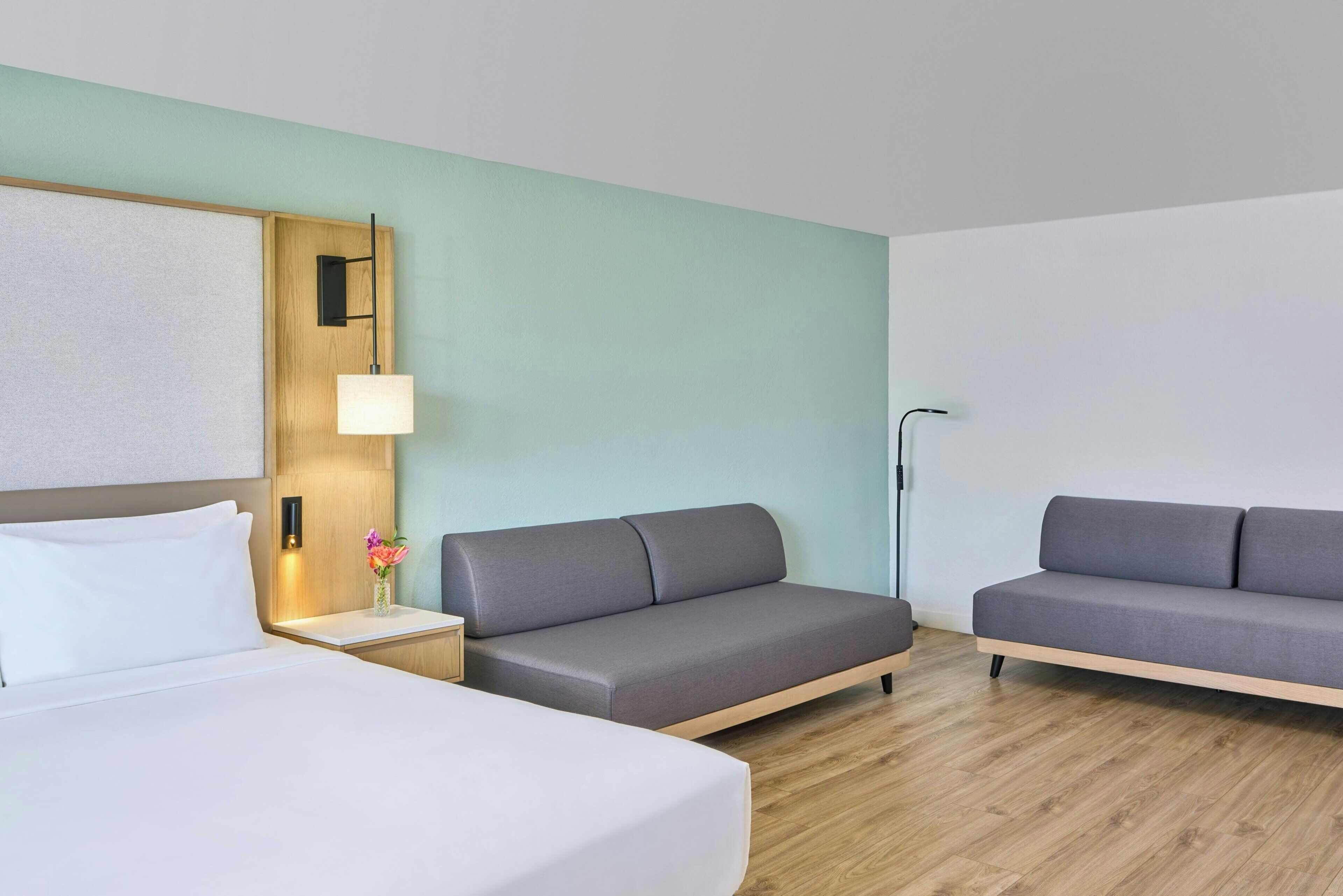 A hotel room with a bed, two sofas, a nightstand with a lamp, and a wall-mounted light fixture.
