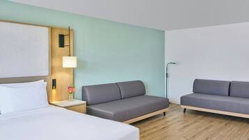 A hotel room with a bed, two sofas, a nightstand with a lamp, and a wall-mounted light fixture.