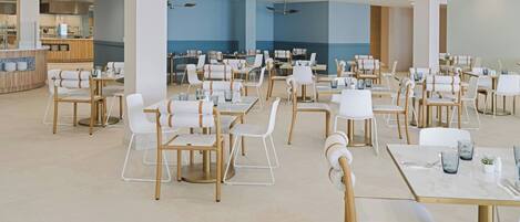 A spacious dining area with multiple tables and chairs, a counter with a beverage station, and a blue accent wall.