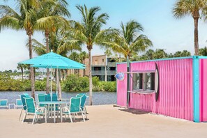 A beachside area with a small kiosk, a table with chairs, and a view of the water and palm trees. - voco Sandpiper All-Inclusive Resort by IHG (Port Saint Lucie)