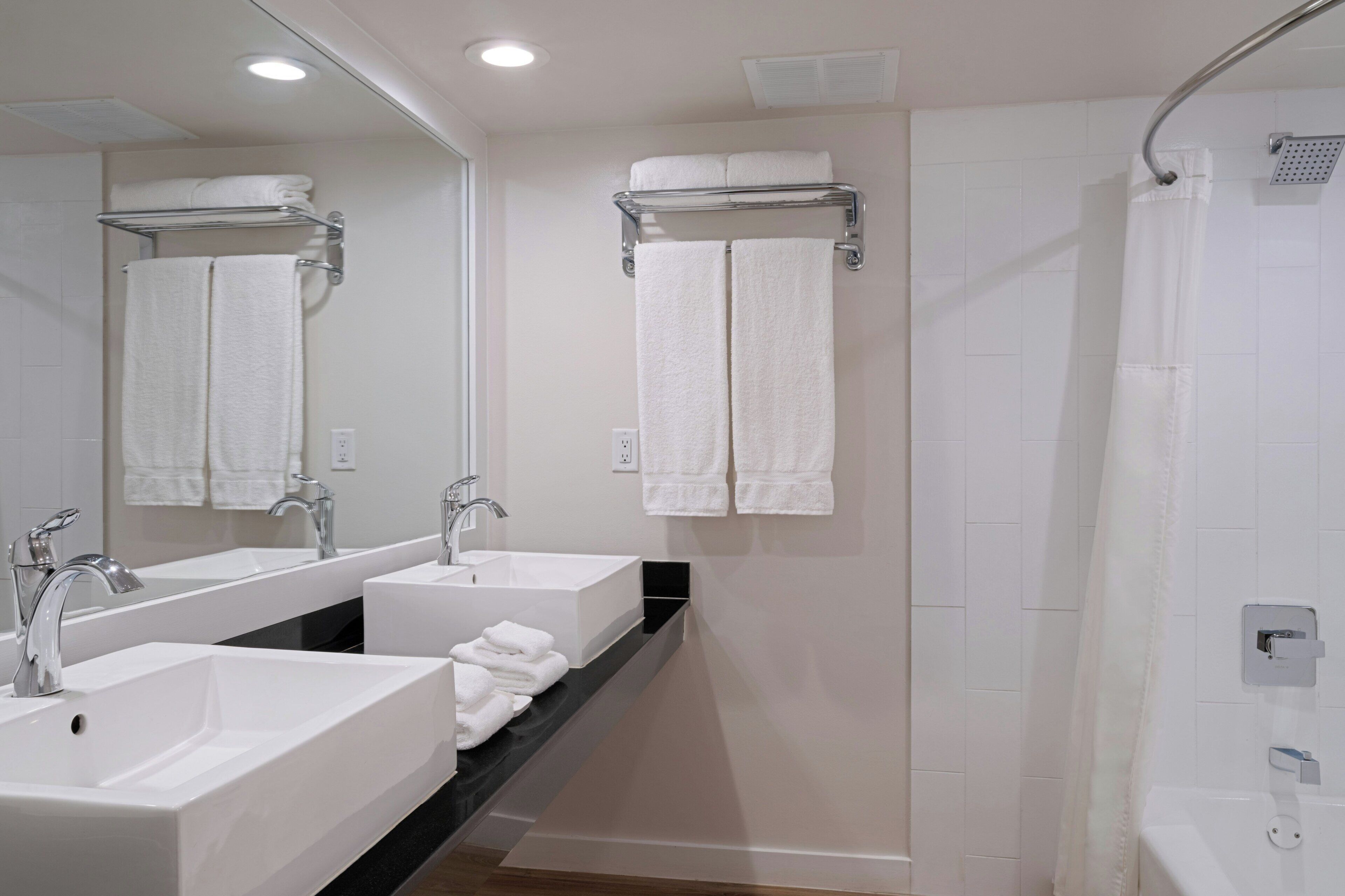 A modern bathroom with two sinks, a shower, and a mirror.