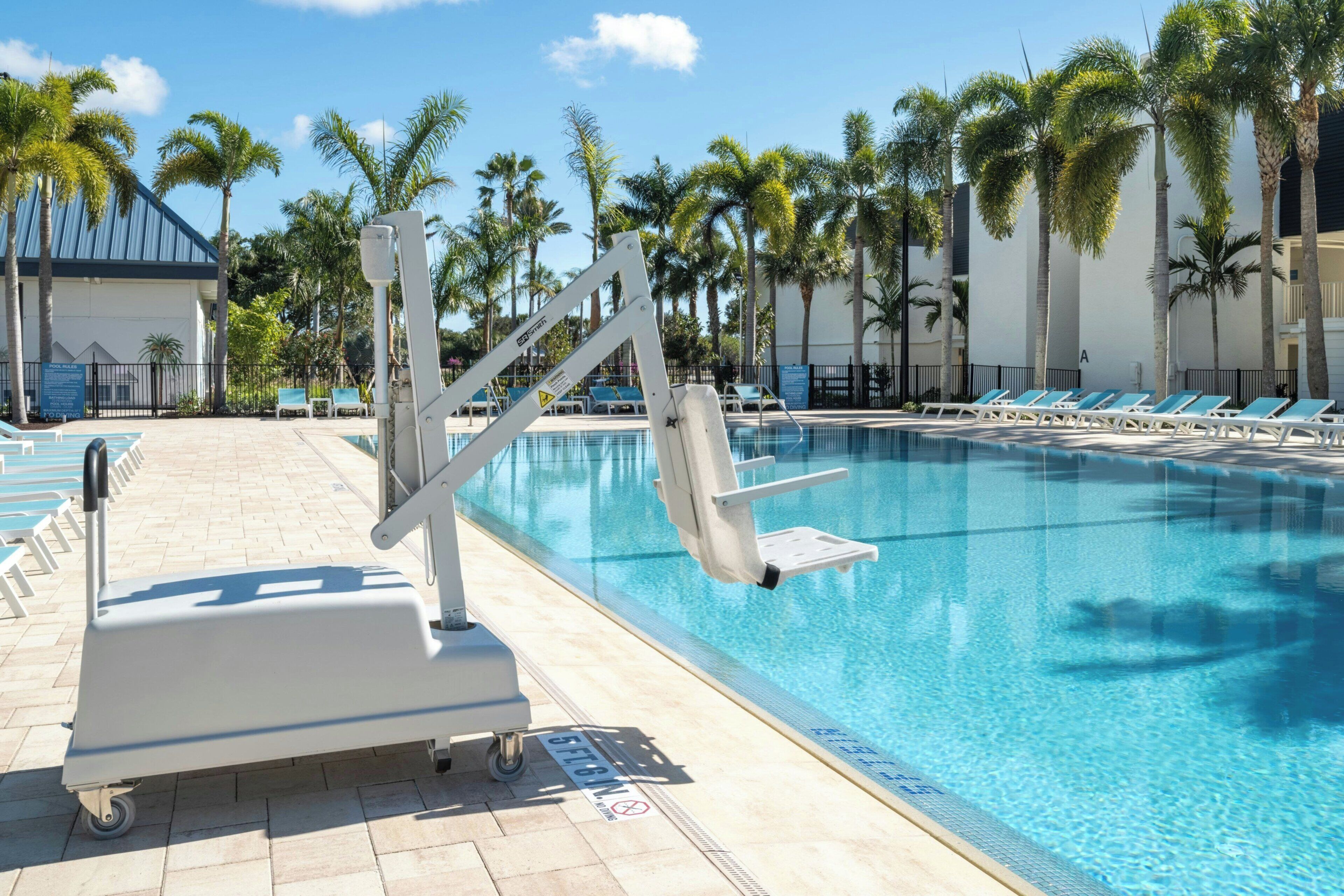 A swimming pool with a diving board, lounge chairs, and palm trees in the background.