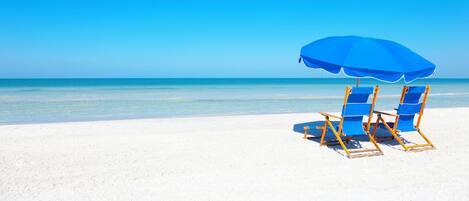 Una playa con dos sillas de playa azules y una sombrilla azul.
