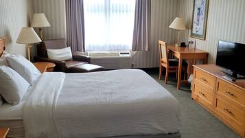Habitación de hotel con una cama grande, un escritorio, una silla, un televisor y una ventana con cortinas.