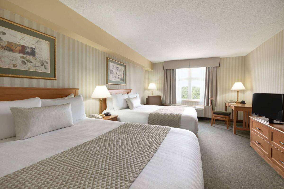 Ein Hotelzimmer mit zwei Betten, einem Schreibtisch, einem Fernseher und einem Fenster mit Vorhängen.