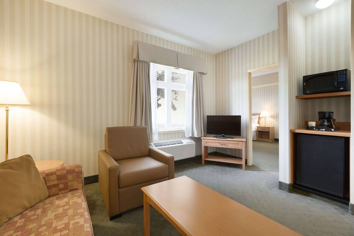 Ein Hotelzimmer mit Sofa, Sessel, Fernseher, kleinen Tisch und einer Küchenzeile.