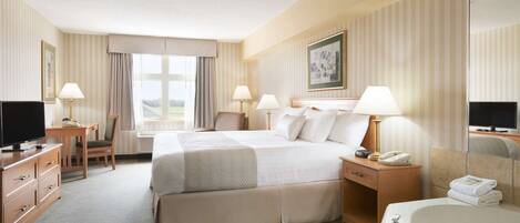 A hotel room with a bed, a desk, a chair, a TV, a lamp, a telephone, and a bathroom with a bathtub and towels.