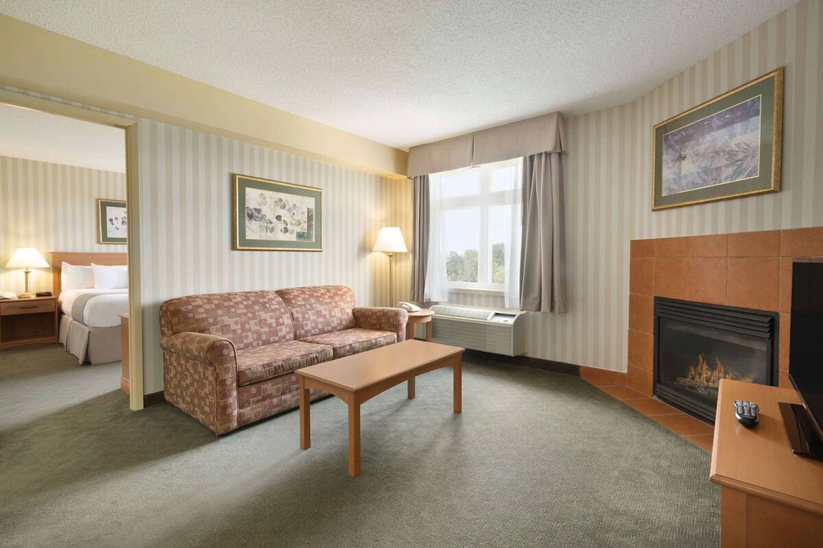 Ein Hotelzimmer mit einer Couch, einem Tisch, einem Kamin, einem Bett und einem Fenster mit Vorhängen.