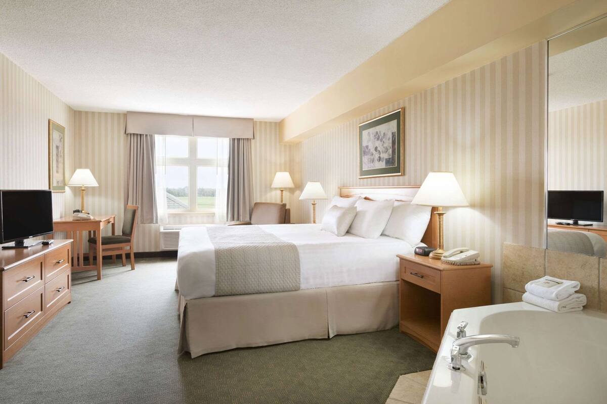 Ein Hotelzimmer mit Bett, Schreibtisch, Stuhl, Fernseher, Lampen und einem Badezimmer.