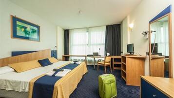 Ein Hotelzimmer mit Bett, Schreibtisch, Stuhl und einem grünen Koffer.