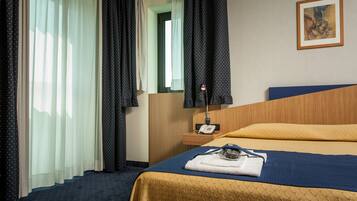 A hotel room with a bed, a bedside table with a lamp, a telephone, and a painting on the wall.