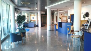 Un vestíbulo amplio con una recepción, zonas de estar y grandes ventanales.