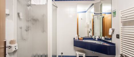 A bathroom with a glass shower enclosure, a white toilet, a sink with a blue countertop, and a mirror above the sink.