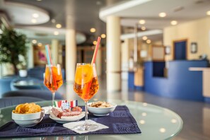 A table with a glass of orange juice, a glass of red wine, a bowl of chips, and a plate of meatballs, set on a glass table in a hotel lobby. - Hotel Mastai (Senigallia)