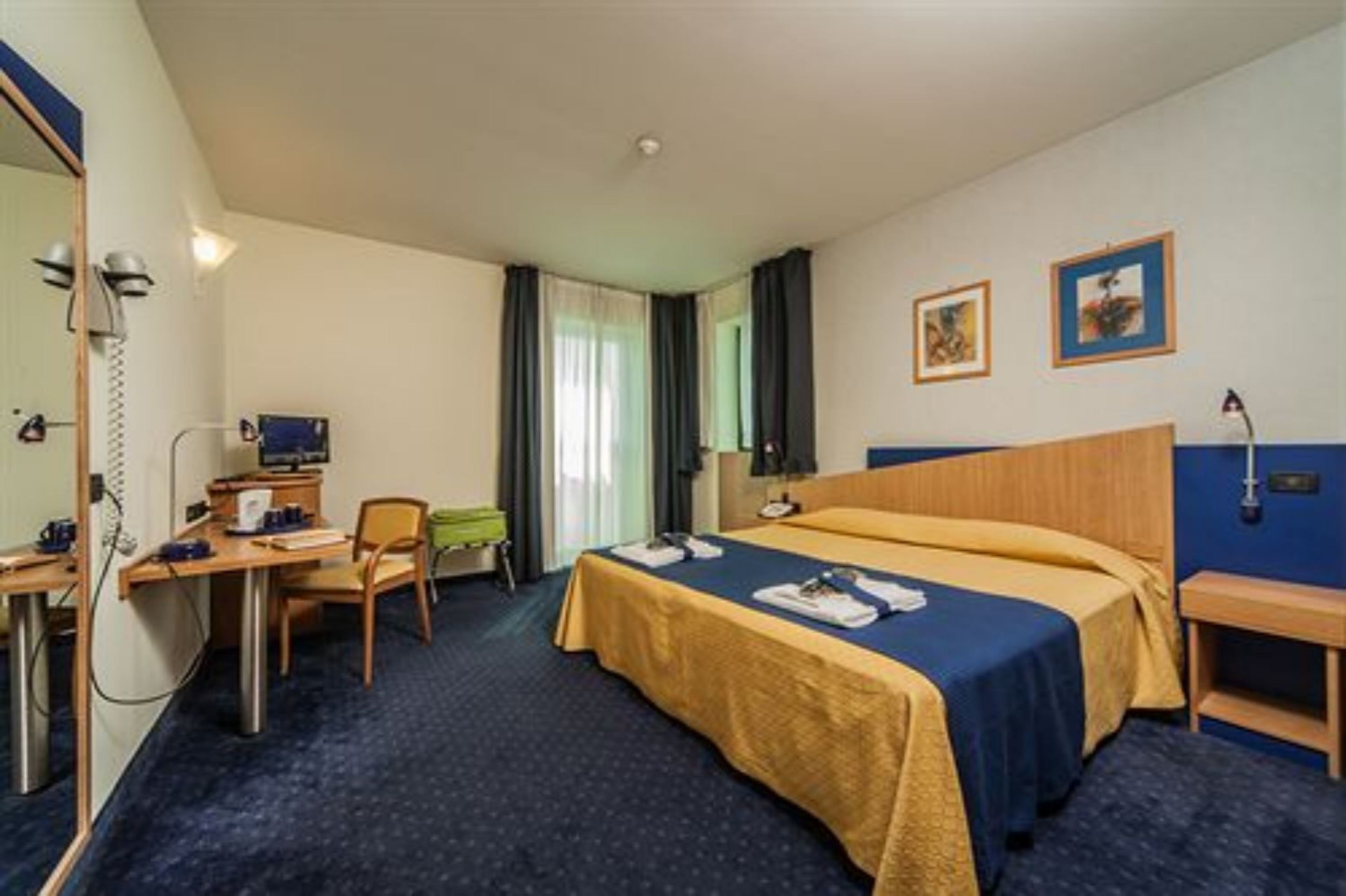 A hotel room with a bed, desk, chair, and a small table.