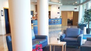 Un vestíbulo con una mesa redonda de vidrio, asientos azules y una zona de recepción al fondo.