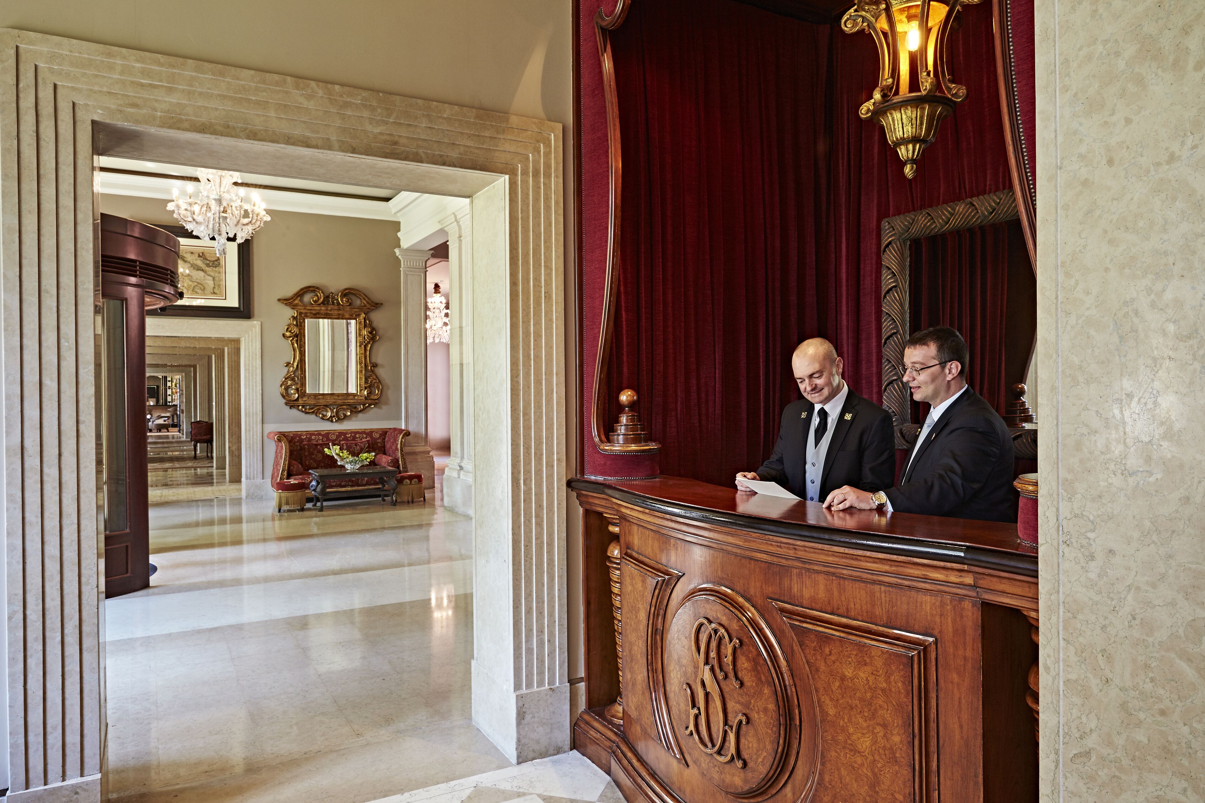 A reception area with a wooden desk, a red curtain, and a chandelier.