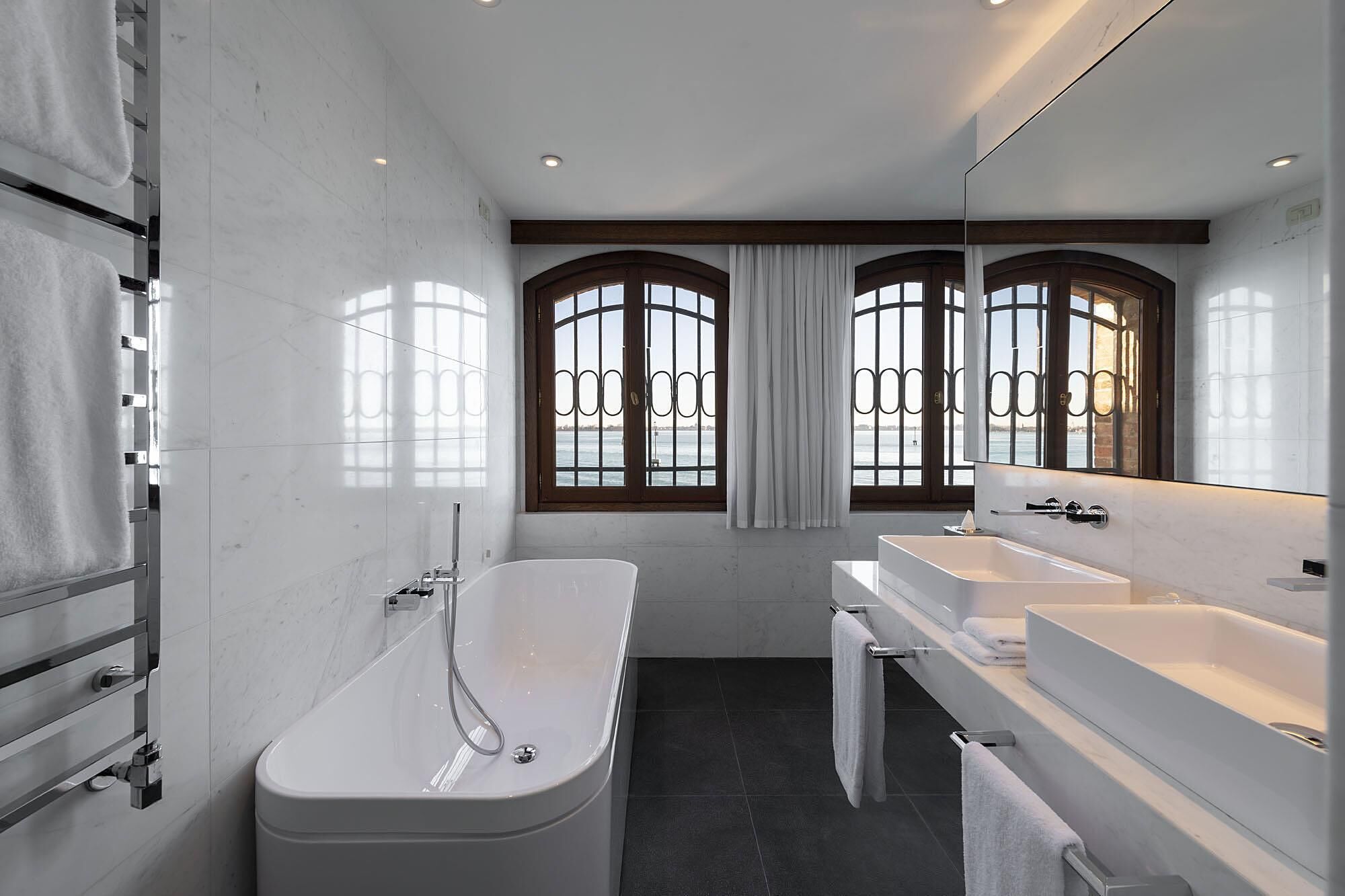 A modern bathroom with a freestanding bathtub, two sinks, and large windows with decorative iron bars.