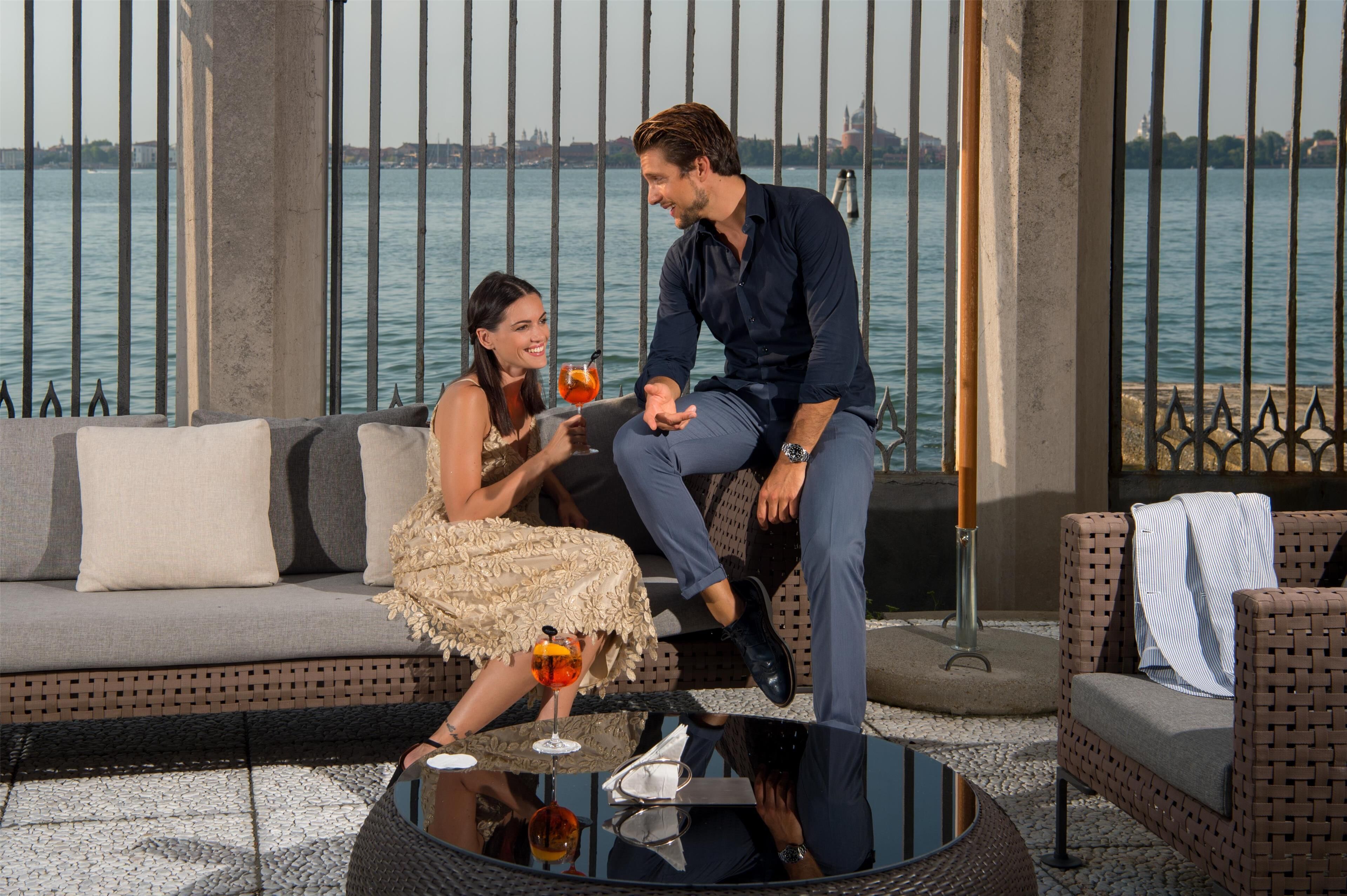 A couple seated on a sofa with a view of a body of water and a cityscape.
