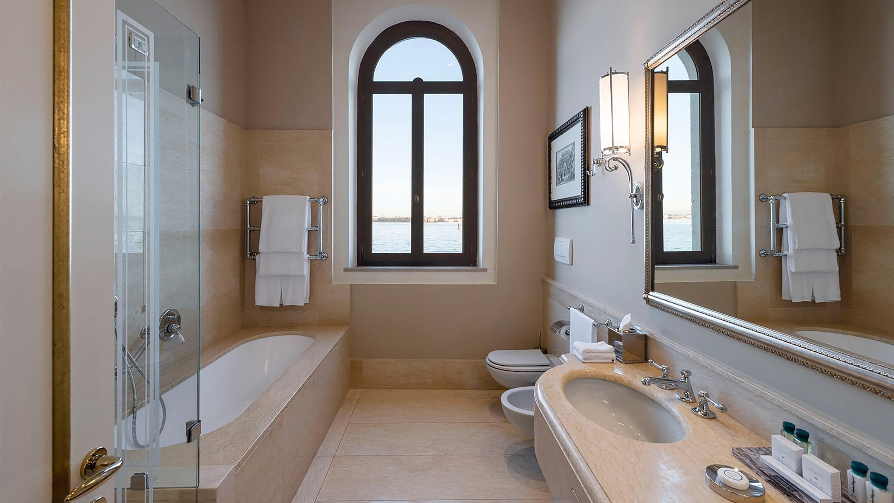 Un baño con bañera, lavamanos e inodoro. Hay una ventana con vistas al exterior.