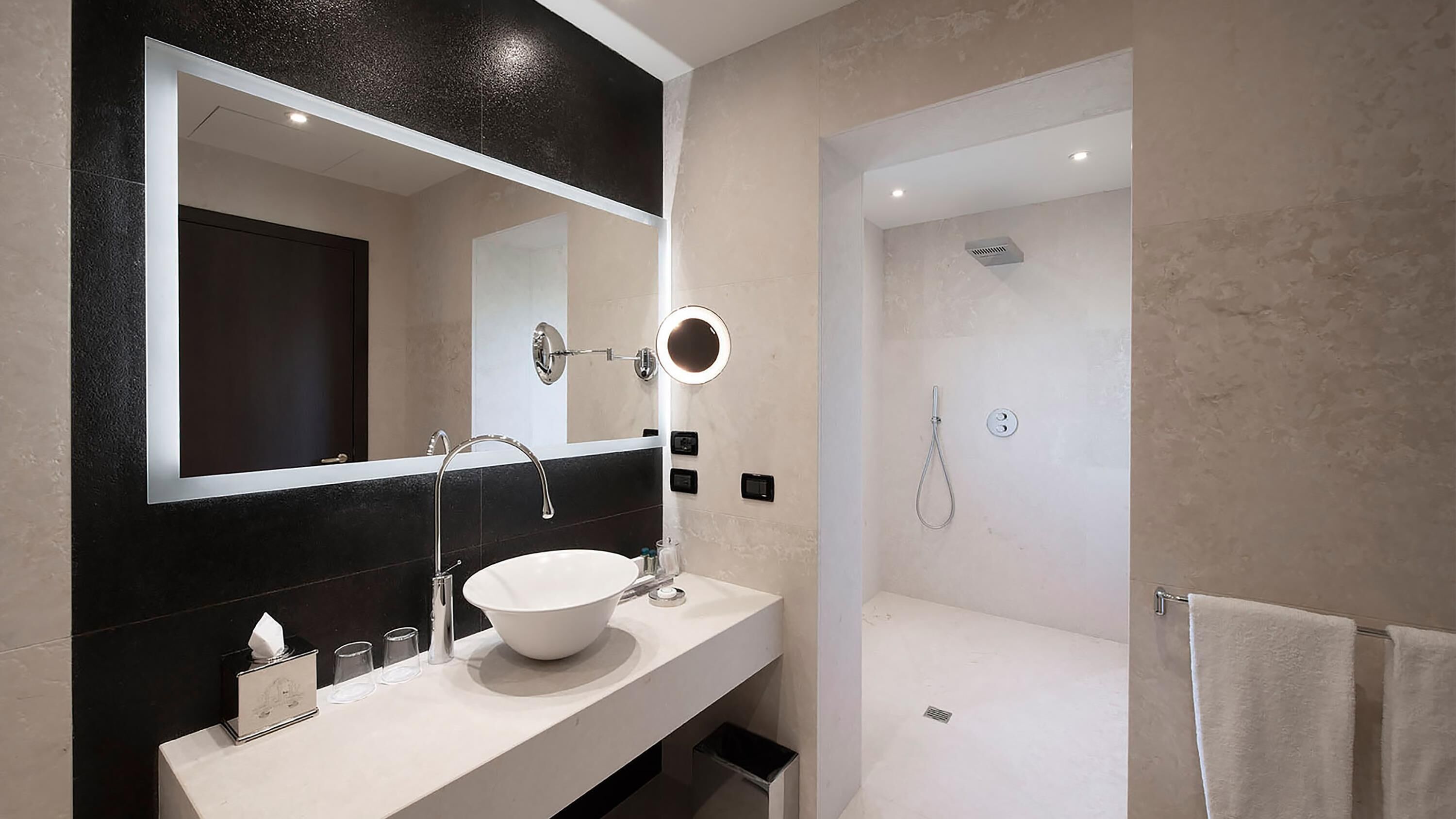 A modern bathroom with a large mirror, a white sink, and a shower.