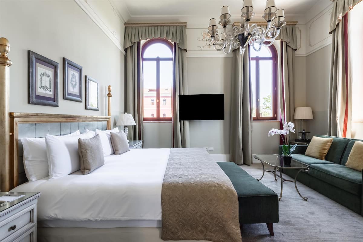 A hotel room with a large bed, a sofa, a TV, and a chandelier.