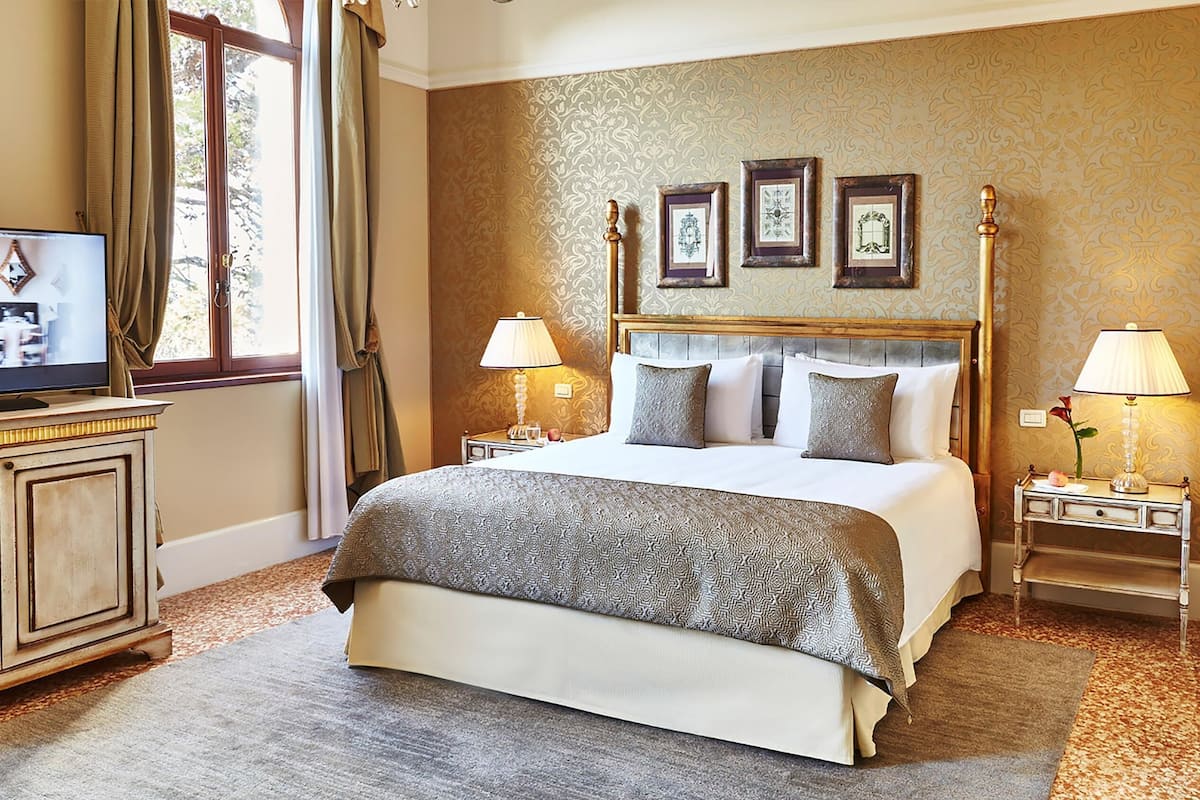 A hotel room with a large bed, two bedside tables with lamps, a television, and framed pictures on the wall.