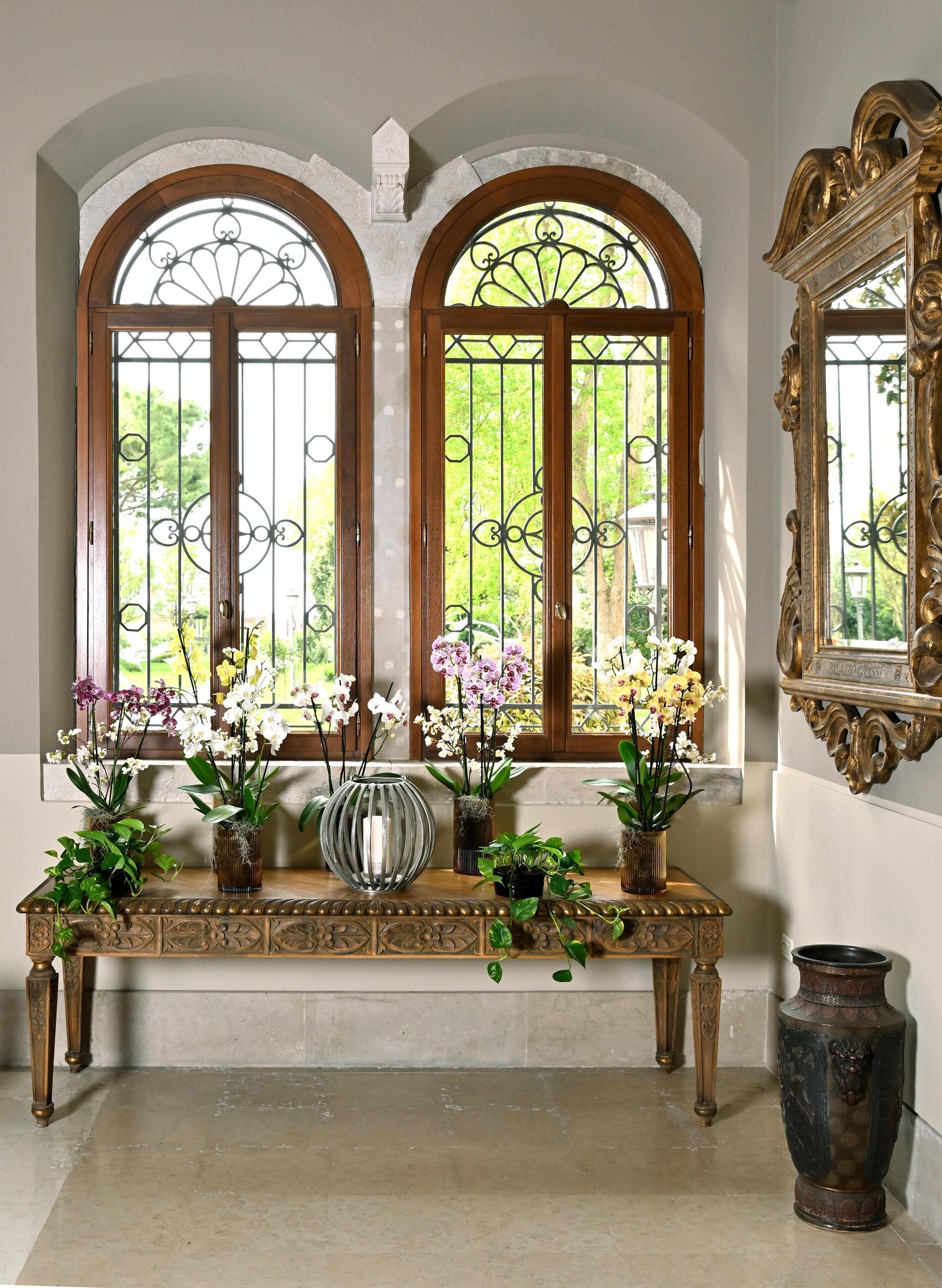 A room with a wooden bench, ornate mirror, and three arched windows with metal grilles.