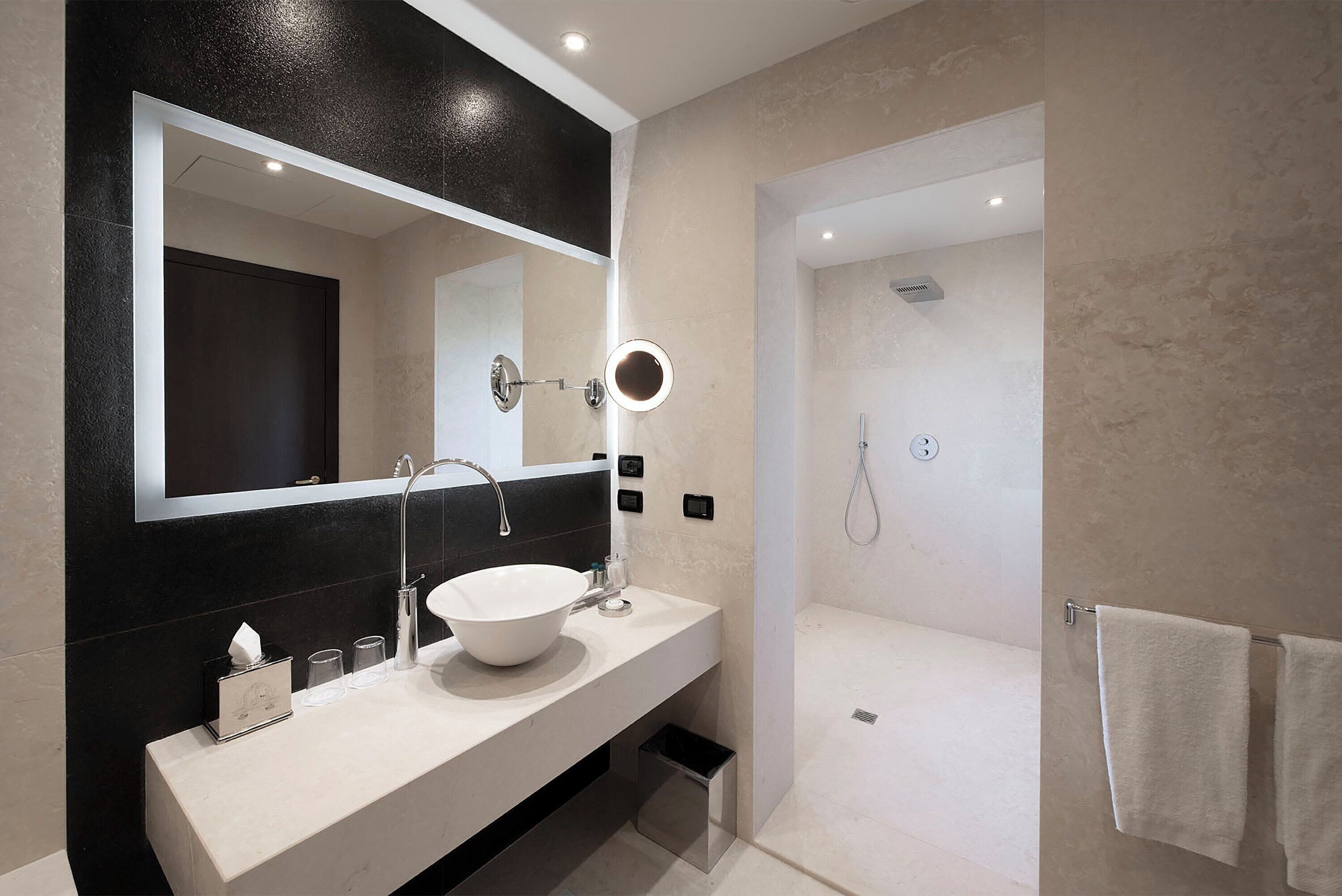 A modern bathroom with a white sink, a large mirror, and a separate shower area.
